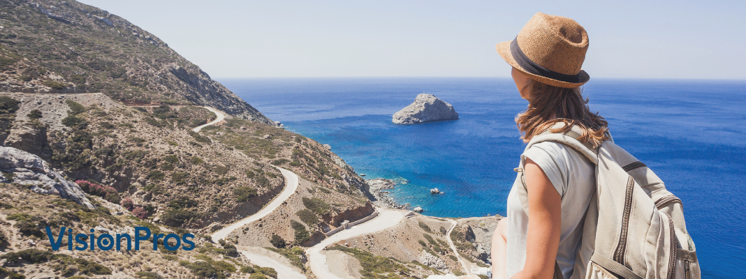 Traveler wearing a hat and backpack looking over a coastal cliff and blue ocean, with VisionPros logo on the left.