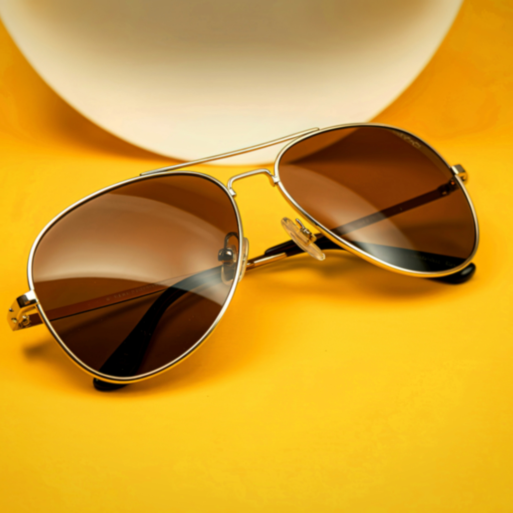 Gold-frame aviator sunglasses with brown lenses on a yellow background
