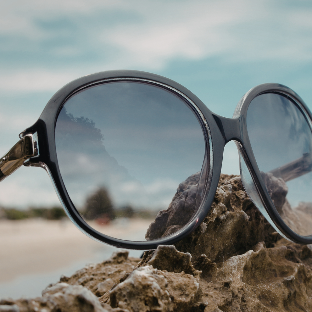 Oversized sunglasses resting on a rock with a beach and cloudy sky in the background