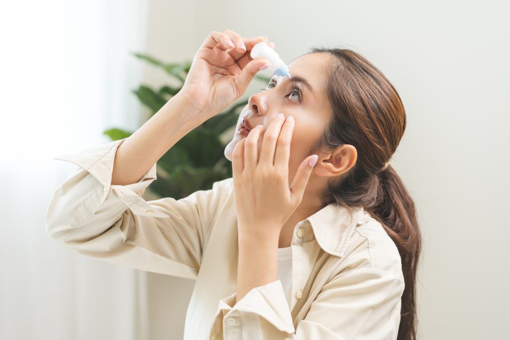 Woman tilts head back and applies eye drops while gently pulling down her lower eyelid.