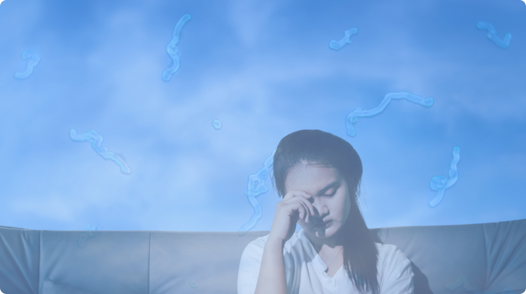 Person sitting on a couch rubbing an eye, with translucent “floaters” drifting across the view to show eye floaters.